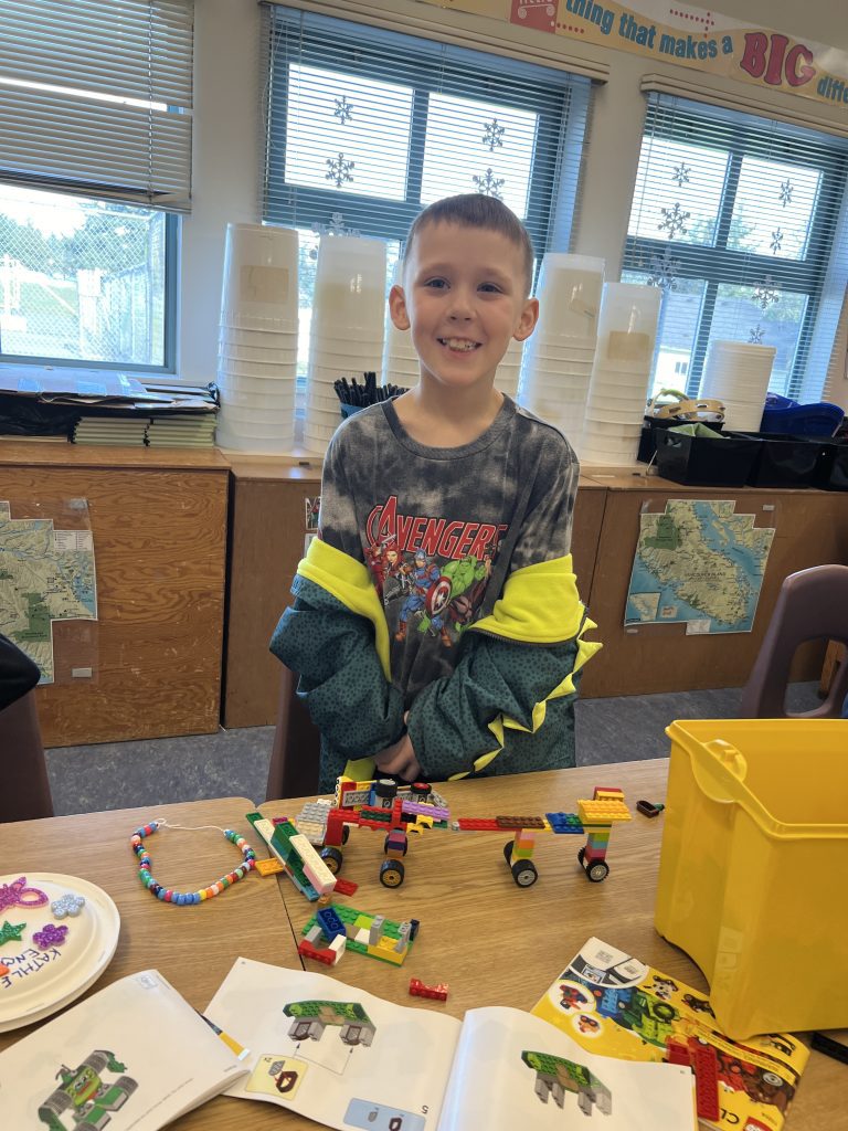 A young boy smiles for a photo eagerly behind the table with his lego creation