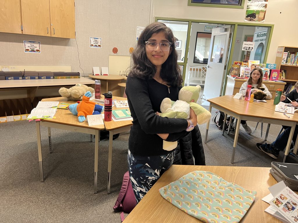 a middle-school aged girl holds a stuffed frog with a diaper on it as if it's a baby