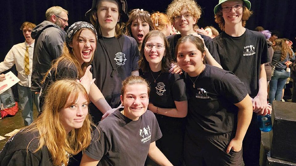 Group of improv students posing for a photo in matching black shirts with a white logo on the top left 